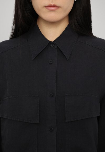 Black button-up shirt made of textured fabric, featuring a classic collar and two front pockets with button closures.