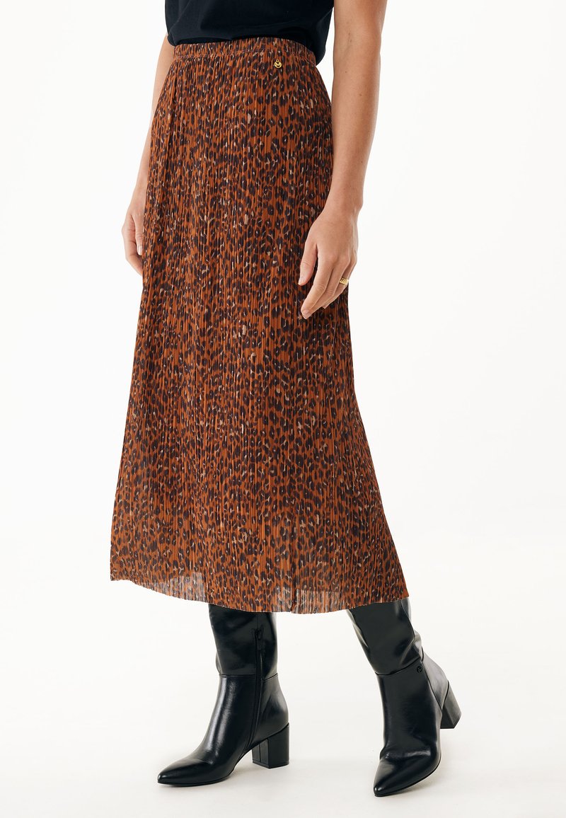 Jupe plissée à imprimé léopard marron avec une taille ajustée et un design fluide, associée à des bottes noires à talons avec un bout pointu.