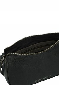 Borsa a mano in pelle nera con superficie testurizzata, dotata di una cerniera argentata, un interno foderato in tela e un logo del marchio discreto sul lato.