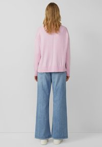 Hellrosa übergroßer Pullover mit gerippten Bündchen und Saum, kombiniert mit weit geschnittenen hellblauen Jeans und weißen Sneakers.