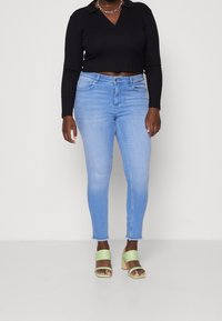 Svart kortärmad polo-topp med v-ringning, tillsammans med ljusblå skinny jeans och gröna klacksandaler med öppen tå.