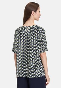 Koszulka z krótkim rękawem w granatowo-kremowo-zielonym wzorze fal; posiada okrągły dekolt i marszczony tył.