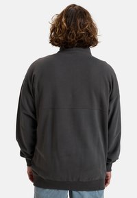 Sweatshirt à capuche gris foncé, avec un col haut, des poignets côtelés et un design de dos sans couture avec une couture horizontale subtile.