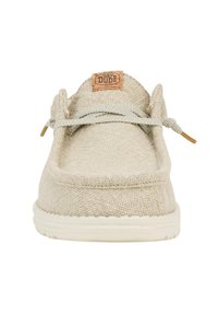 Scarpa slip-on in tela beige con superficie testurizzata, suola in gomma crema e un'etichetta in cuoio marrone con la scritta "HEY DUDE" sulla linguetta.