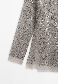 Long tissu argenté couvert de sequins avec une bordure en dentelle transparente sur les bords, montrant des détails complexes et scintillants.