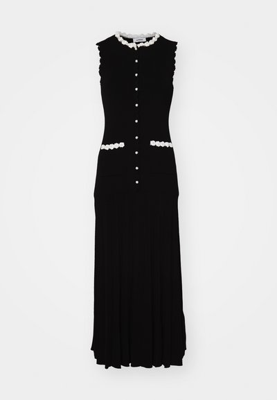 Juodas be rankovių suknelė su prigludusiu liemeniu, balta gėlių apdaila ir mygtukais. Yra dvi priekinės kišenės ir klostuota sijono dizainas.