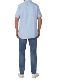 Lichtblauwe shirt met korte mouwen, comfortabele pasvorm, rugplooidetail, gecombineerd met vervaagde spijkerbroek en witte sneakers met beige zolen.