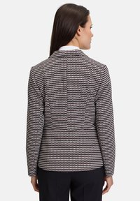 Veste sur mesure en tissu texturé avec un motif pied de poule noir, crème et bordeaux. Col cranté et manches longues.