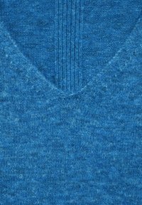 Närmre bild av blått stickat tyg med V-ringning och ribbat mönster i mitten.