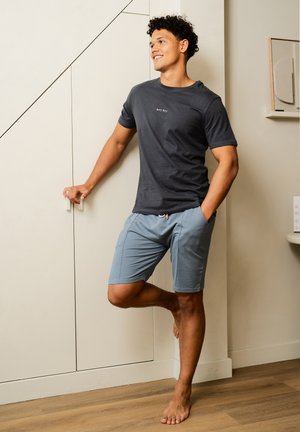Graues T-Shirt mit "hey hey"-Text, kombiniert mit hellblauen Shorts. Der Stoff wirkt weich und lässig, mit einem lockeren Schnitt.