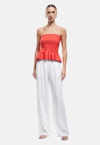 Top peplum rojo sin tirantes con un corsé ajustado y dobladillo acampanado, combinado con pantalones anchos blancos, acompañado de zapatos de tacón abierto.