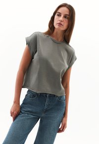 Olivengrønt cropped t-shirt med korte, rullede ærmer og synlige sømme, parret med højtaljede blå jeans. Casual bomuldsstof.