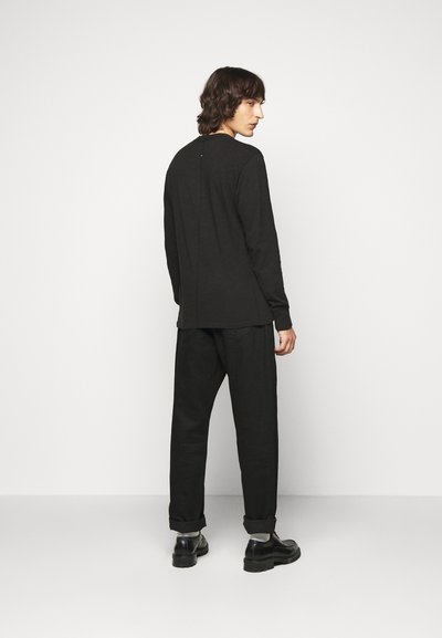 Black long-sleeve shirt and matching loose trousers, made of textured fabric. Features a back seam detail and rolled cuffs. Black shoes complete the look.