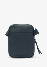 Tamno plava crossbody torba s teksturiranim finišem, pravokutnog oblika, i prednjim džepom. Ima zatvaranje na zip i podesivu naramenicu.