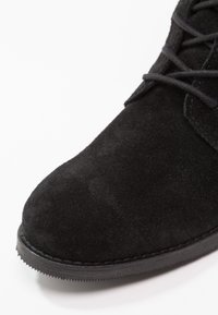 Stivaletto in suede nero con punta arrotondata, dotato di lacci neri e suola in gomma testurizzata. L'ingrandimento mostra una finitura liscia e opaca.