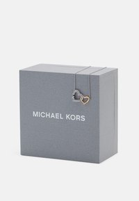 Hallitus halli tekstuuriga karp, millel on "MICHAEL KORS" logo. Õhuke ahel on kinnitatud kahetoonilise südame ripatsi külge, üks hõbedane ja teine kuldne.