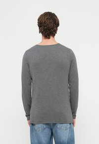 Siva majica z dolgimi rokavi iz mehkega blaga, z okrolim izrezom in sproščenim krojem, kombinirana s svetlo modrimi kavbojkami.