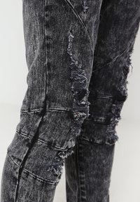 Czarne dżinsy o zniszczonym wzorze z postrzępionymi łatami, textured powierzchnią i wieloma nacięciami wzdłuż nóg.