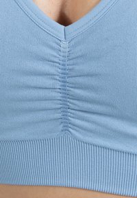 Lichtblauwe aansluitende bralette met een V-hals, geribbeld textuur en geplooide details in het midden. Zachte stof met een strakke band aan de onderkant.