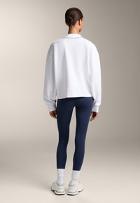 Bela oversize jutka s krožnim izrezom, v kombinaciji z mornarsko modrimi leginami. Obutev so svetle tenisice z detajli.