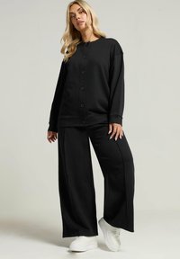 Conjunto de ropa de estar en negro que incluye una blusa de botones de manga larga con mangas anchas y pantalones de pierna ancha a juego, ambos en una tela suave y con un corte relajado.