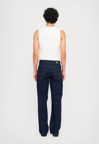 Temno modri jeans z ravnim krojem, okrašeni z oranžnimi šivi in dvema zadnjima žepoma. Nosi se z belim topom brez rokavov.