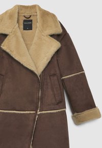 Manteau en similicuir marron avec col en fausse fourrure beige, fermeture éclair, poches latérales et accents beiges le long des manches et de l'ourlet.