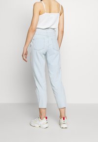 Ljusblå jeans med hög midja och avsmalnande ben. Bakfickor synliga, kombinerade med vita sneakers med röda detaljer. Minimalistisk design.