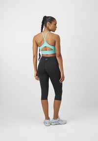 Reggiseno sportivo blu chiaro con design a taglio e spalline regolabili abbinato a leggings neri a tre quarti. Scarpe da ginnastica grigie completano l'outfit.