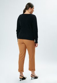 Sort lodden sweater, brune tilspidsede bukser og sorte slingback hæle med pynt. Enkel silhuet med opsmøgede manchetter og blød tekstur.