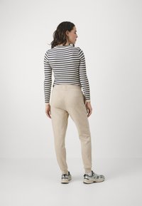Stripet langermet topp i marineblå og krem, parret med beige joggebukser. Joggebuksene har elastisk midje og ribbede ankler.