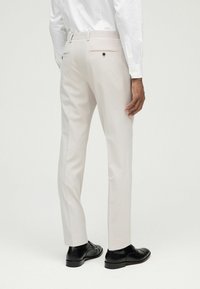 Pantalones tailored de un beige claro con corte slim, que cuentan con dos bolsillos traseros y una textura suave, combinados con zapatos de vestir negros.