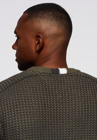 Suéter de punto en verde oscuro con tejido texturizado, cuello acanalado verde y acento de tres colores en la parte posterior del cuello.