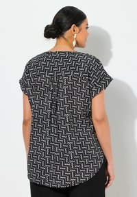 Top a maniche corte con motivo a zigzag bianco e nero, orlo arrotondato e dettaglio del bottone sul retro, realizzato in tessuto leggero.