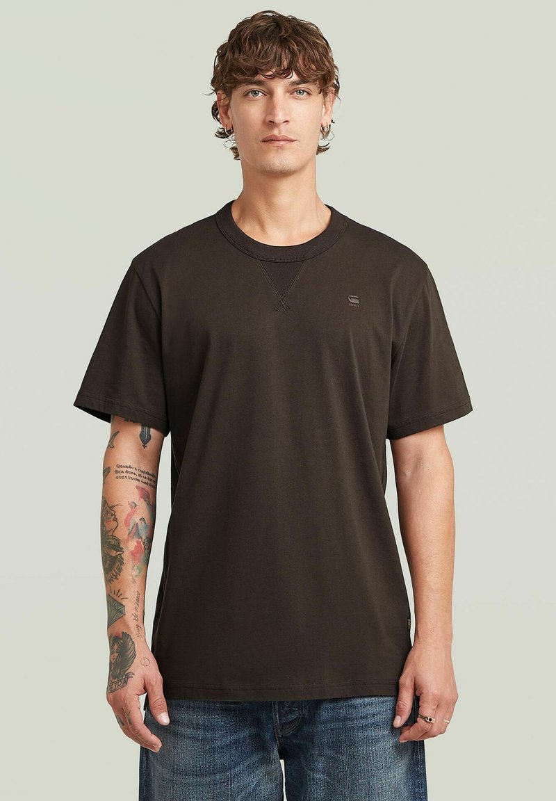 T-shirt in cotone marrone scuro con collo rotondo, maniche corte e un piccolo logo sul petto. Vestibilità ampia con una texture liscia.