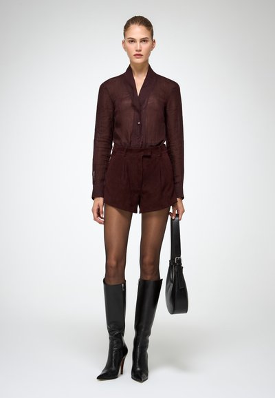 Camicia trasparente bordeaux con bottoni, abbinata a pantaloni corti bordeaux in suede a vita alta. Stivali neri al ginocchio e una piccola borsa nera completano il look.