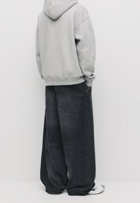 Harmaa huppari rentotilassa, yhdistetty tummiin denimin leveälahkeisiin housuihin. Housuissa on kaksoistaskut selässä ja sileä pinta.