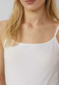 Weiße, dünn-träbige Spaghetti-Top aus weichem Stoff. Glatte Textur mit einfachem Design, eng anliegend am Hals und den Schultern.