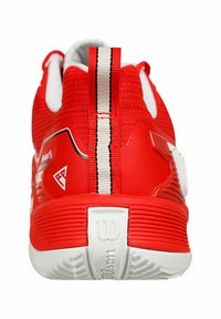 Scarpa sportiva rossa con superiore in maglia strutturata, dettagli bianchi e un'etichetta a strisce. Presenta una suola in gomma rigata e un logo sul tallone.