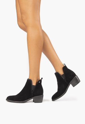 Stivali alla caviglia in suede nero con tacco basso e inserti elastici laterali. Presentano una superficie testurizzata e una piccola linguetta sul retro.