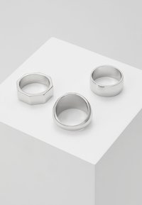 Três anéis de prata com designs variados: um anel octagonal, um anel arredondado e suave, e um anel de lados planos, todos com um acabamento polido.