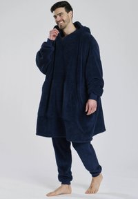 Marineblå oversized hoodie lavet af plyssstof med en frontlomme, lange ærmer og matchende bukser. Blød, struktureret overflade hele vejen igennem.
