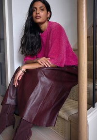 Fuksijos spalvos puri mezginė megztinė, ruda odinė sijonas su blizgiu paviršiumi, derinamas su bordo zomšos aukštakulniais aulinukais. Šilta neutrali fonas.