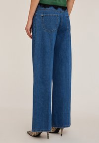 Vatsakankaiset siniset farkut, joissa on raaka helma, kahdella takataskulla ja kontrastikankaalla. Tekstuurin ilme on tukeva ja hieman haalistunut.