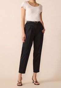 Czarne spodni z wysokim stanem, z zakładkami i kieszeniami; zestawione z dopasowaną białą bluzką z okrągłym dekoltem i czarnymi sandałami na obcasie.
