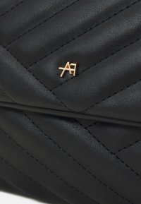 Svart quiltad läderväska med en guldfärgad logotypdetalj. Den har diagonal sömnad och en slät, texturerad yta.