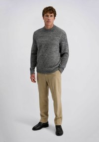 Grijze gebreide trui met een ronde hals, gecombineerd met beige broek en zwarte schoenen. De trui heeft subtiele textuurvariaties.