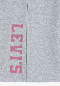 Pelēka kokvilnas krekla ar lielu rozā "LEVI'S" logotipu sānos. Audums izskatās mīksts, un dizains ir ikdienišķs un vienkāršs.