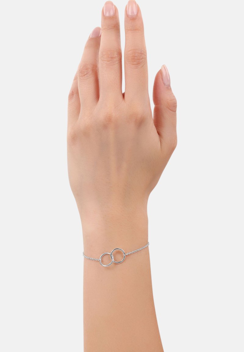 Pulsera de cadena de plata con dos círculos enlazados como punto focal. Textura suave y diseño minimalista, llevada en una mano de tono de piel claro.