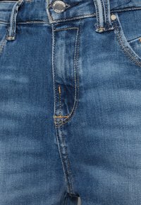 Jeans i denim i mellanblå färg med en urvattnad finish, utrustad med orange sömmar, en framficka och en metallknappstängning i midjan.